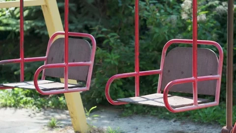 Empty red garden swings hanging beneath trees Stock Footage 346714070