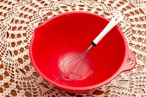Empty red plastic bowl with egg whisk. Crochet tablecloth background Stock Photos