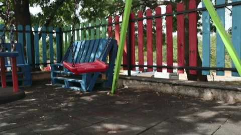 Empty Red Swing Moving Gently on a Colorful Playground Stock Footage 345144167