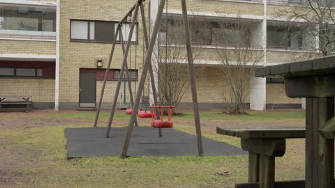Empty red swings moving in playground outside residential brick building 스톡 동영상 326125176
