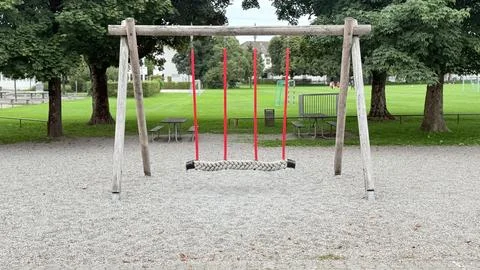Empty red swings in playground surrounded by green trees outdoor Stock Photos