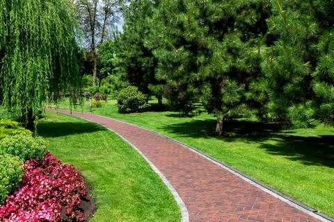 Empty red tile footpath in well maintained park with a green spaces. Stock Photos