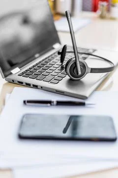 Empty remote office workplace with laptop pc, phone, headset and papers closeup Stock Photos