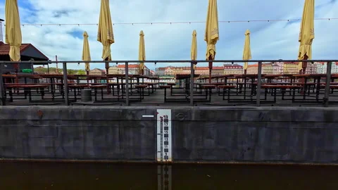 Empty restaurant benches and umbrellas over Czechia, Prague river depth gauge Stock Footage 296790592