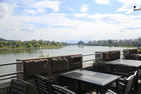Empty riverside patio tables overlooking a broad river with distant bridge .. Foto stock