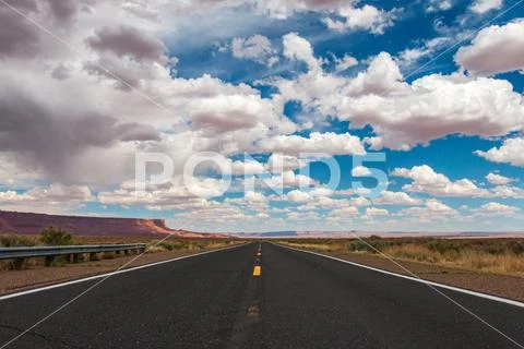 Empty road in the Arizona desert with big clouds and blue sky Stock Photos
