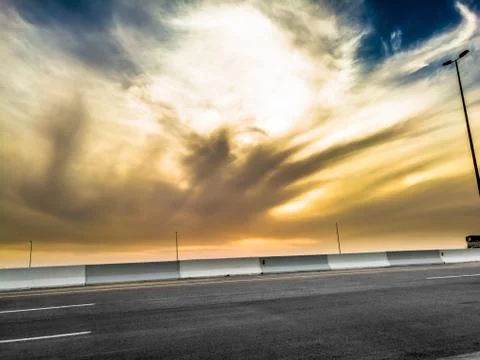 An empty road dramatic clouds on the sky and street lights in the background Stock Photos