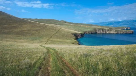 An empty off road in spacious fields with blue sea Stock Photos