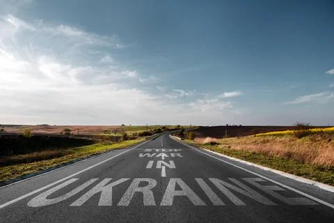 Empty road through the field with the text on the pavement Stop war in Ukraine Stock Photos