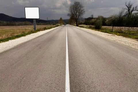 Empty road through fields with blank billboard beside Foto stock