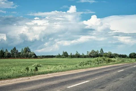 Empty road through the green fields on a cloudy summer day 写真素材