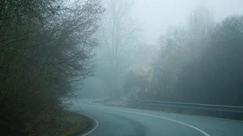 An empty road turns in a misty forest, early winter morning Stock Photos