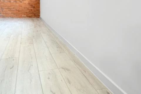 Empty room interior with light wood laminate flooring and white wall with bas Stock Photos