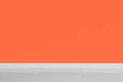 Empty room interior with vibrant orange wall, white baseboard, and gray tiled Stock Photos