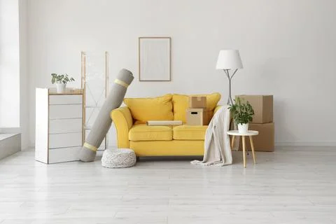 Empty room with yellow sofa, moving boxes, and rolled carpet, new home reloca Stock Photos