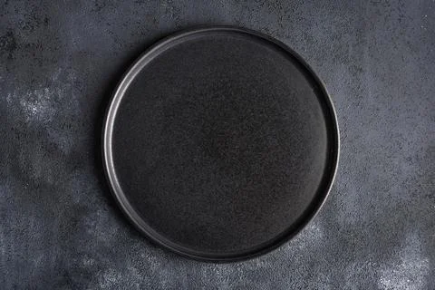 Empty round black plate on dark moody dark background with copy space Foto stock