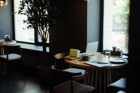 Empty round brown wooden table near window in cafe with laptop, cup of coffee Stock Photos