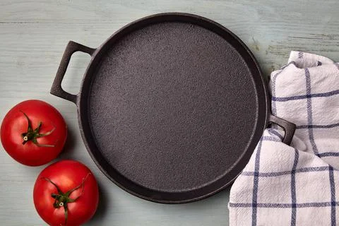 Empty round cast iron pan, tea towel and tomatoes Stock Photos