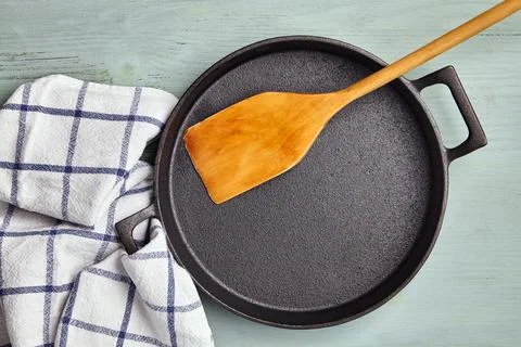 Empty round cast iron pan, wooden spatula, and tea towel napkin Stock Photos