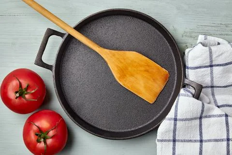Empty round cast iron pan, wooden spatula, tea towel and tomatoes Stock Photos
