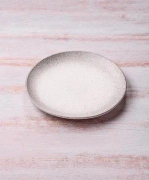 An empty round ceramic plate on a dark, textured white background. An empty.. Stock Photos
