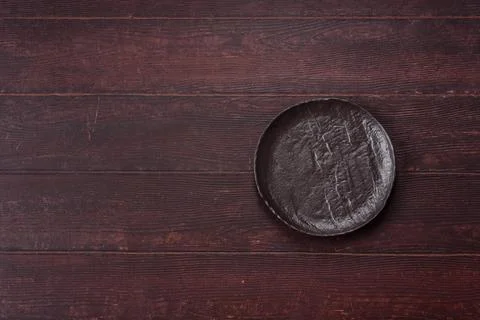 An empty round ceramic plate on a dark, textured brown background. An empty.. Stock Photos