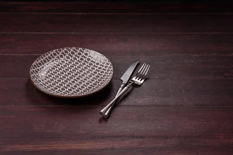 An empty round ceramic plate on a dark, textured brown background. An empty.. Stock Photos