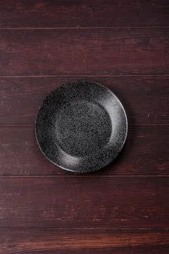 An empty round ceramic plate on a dark, textured brown background. An empty.. Stock Photos