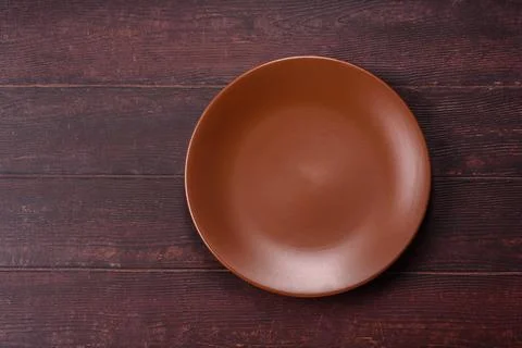 An empty round ceramic plate on a dark, textured brown background. An empty.. Stock Photos