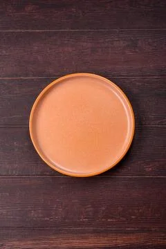 An empty round ceramic plate on a dark, textured brown background. An empty.. Stock Photos