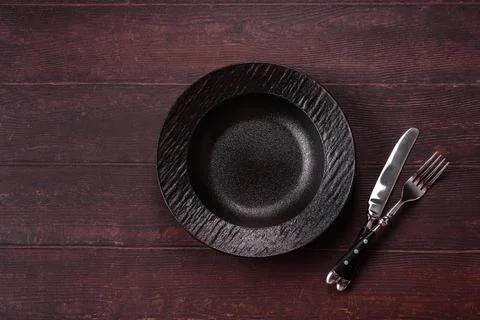 An empty round ceramic plate on a dark, textured brown background. An empty.. Stock Photos