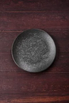 An empty round ceramic plate on a dark, textured brown background. An empty.. Stock Photos