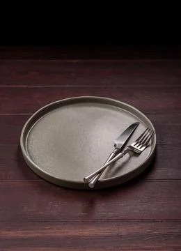 An empty round ceramic plate on a dark, textured brown background. An empty.. Stock Photos