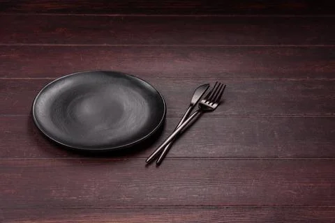 An empty round ceramic plate on a dark, textured brown background. An empty.. Stock Photos