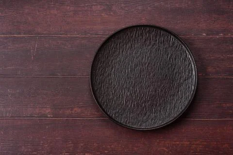 An empty round ceramic plate on a dark, textured brown background. An empty.. Stock Photos