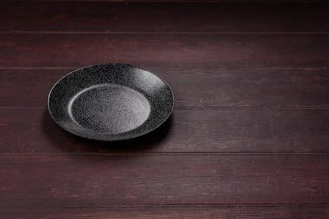 An empty round ceramic plate on a dark, textured brown background. An empty.. Stock Photos