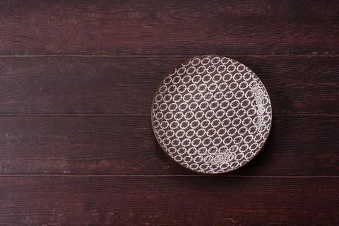 An empty round ceramic plate on a dark, textured brown background. An empty.. Stock Photos