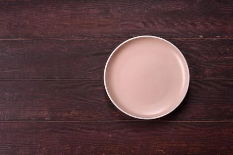 An empty round ceramic plate on a dark, textured brown background. An empty.. Stock Photos