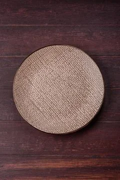 An empty round ceramic plate on a dark, textured brown background. An empty.. Stock Photos