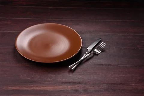 An empty round ceramic plate on a dark, textured brown background. An empty.. Stock Photos