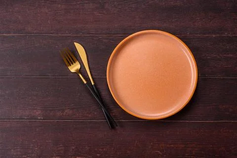 An empty round ceramic plate on a dark, textured brown background. An empty.. Stock Photos