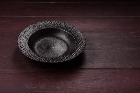 An empty round ceramic plate on a dark, textured brown background. An empty.. Stock Photos
