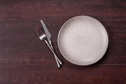 An empty round ceramic plate on a dark, textured brown background. An empty.. Stock Photos