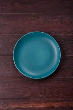 An empty round ceramic plate on a dark, textured brown background. An empty.. Stock Photos