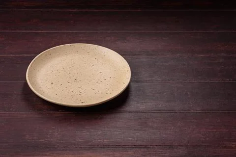 An empty round ceramic plate on a dark, textured brown background. An empty.. Stock Photos