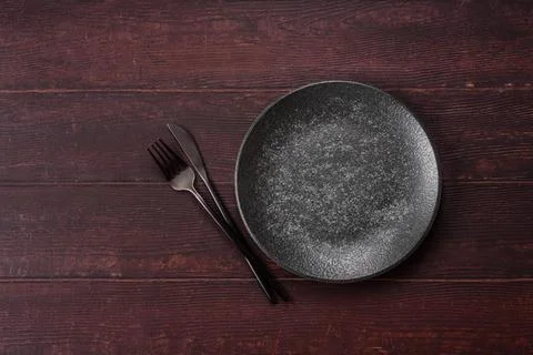 An empty round ceramic plate on a dark, textured brown background. An empty.. Stock Photos