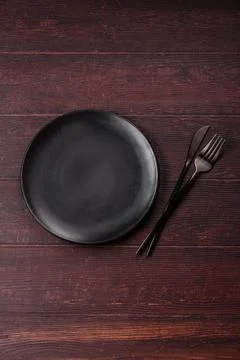 An empty round ceramic plate on a dark, textured brown background. An empty.. Stock Photos