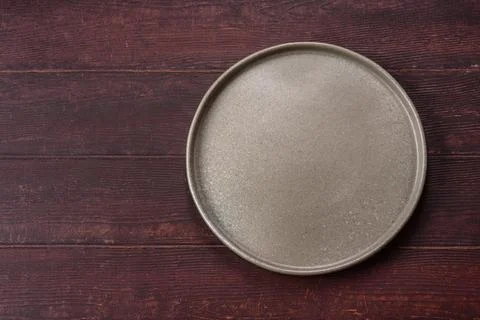 An empty round ceramic plate on a dark, textured brown background. An empty.. Stock Photos