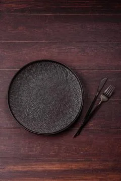 An empty round ceramic plate on a dark, textured brown background. An empty.. Stock Photos