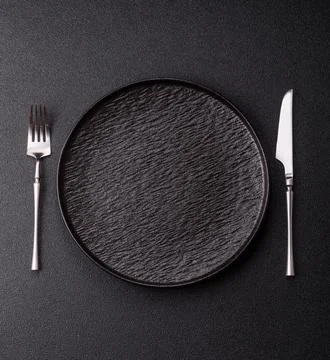 An empty round ceramic plate, knife, and fork as a dining table setting. An.. Stock Photos